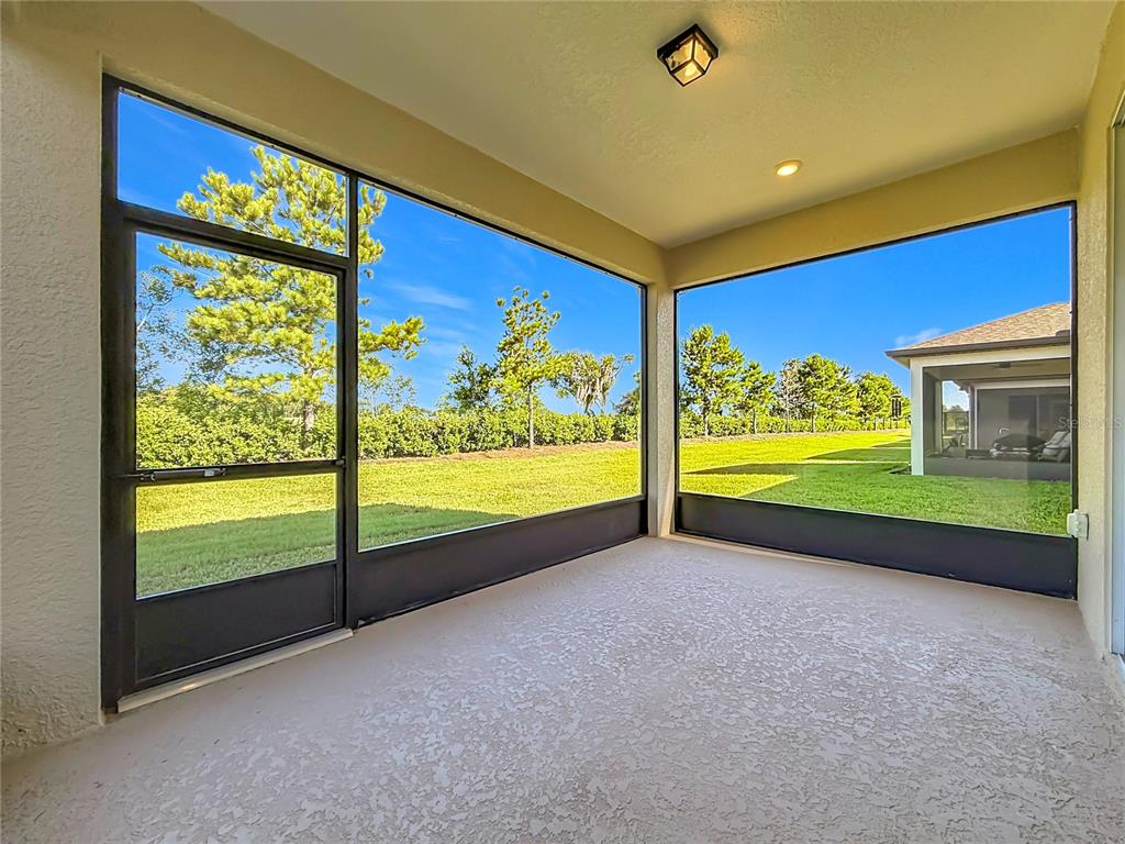 A screened-in patio features a textured concrete floor, a ceiling light, and views of grass — 6046 SW 93RD CIRCLE, OCALA, FL
