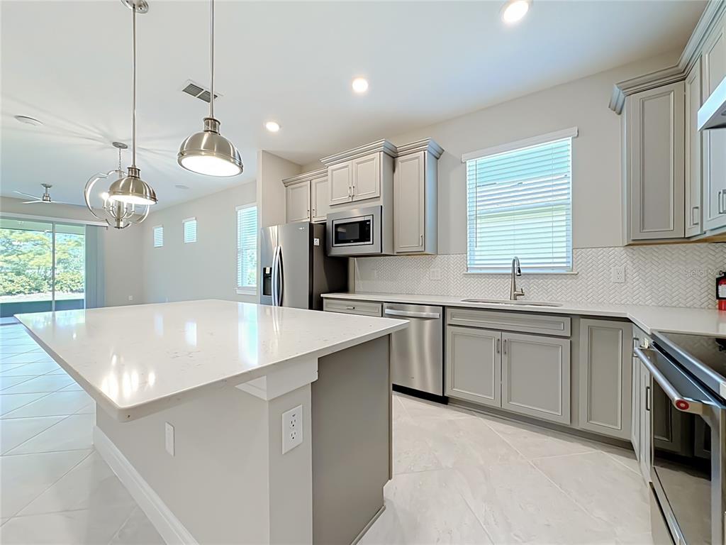 A modern kitchen features light gray cabinets, white quartz countertops, stainless steel appliances, and an island — 6046 SW 93RD CIRCLE, OCALA, FL