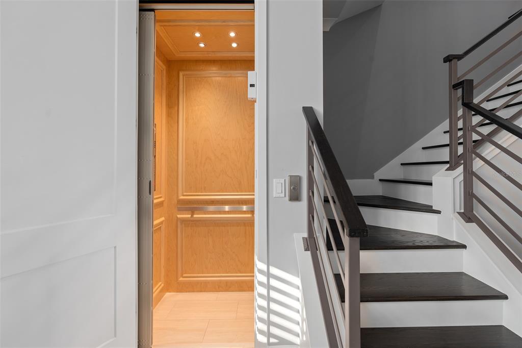 An open wooden elevator sits next to a staircase with dark wood treads and railings — 129 S PARK AVENUE, WINTER GARDEN, FL