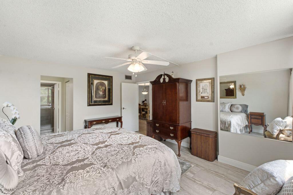 A bedroom features a patterned bedspread, a large wooden armoire, and a wall-mounted mirror — 3801 Environ Boulevard # 318, Lauderhill FL 33319, LAUDERHILL, FL