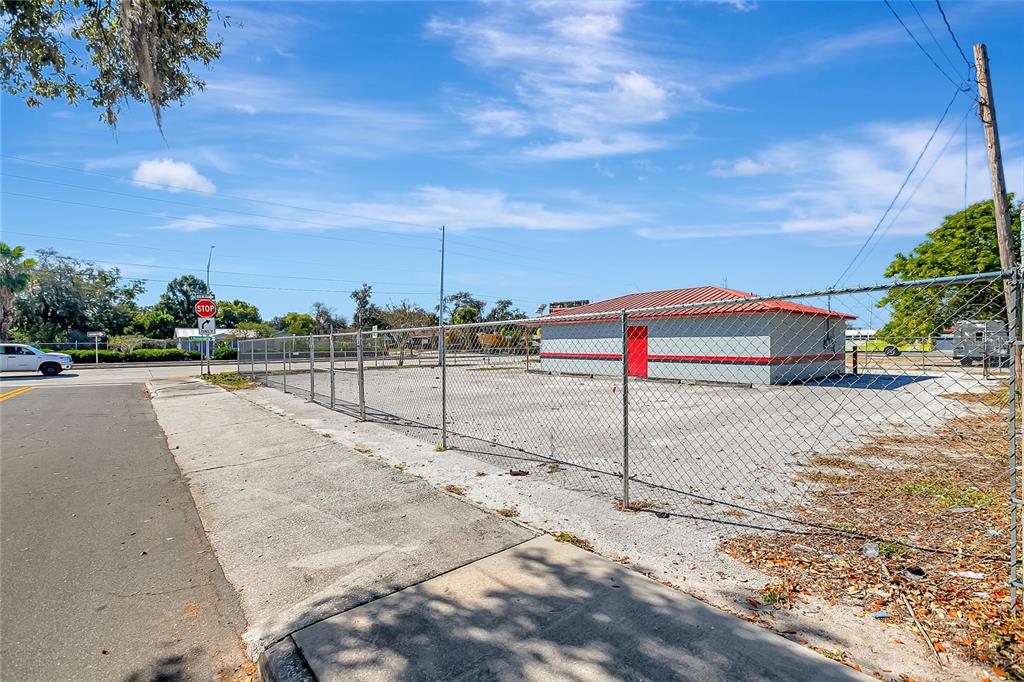 A fenced, vacant lot features a small, single-story building with a red metal roof — 305 & 309 W MEMORIAL BOULEVARD, LAKELAND, FL