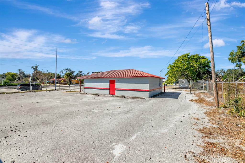 A small, rectangular building with a red metal roof sits in a large, cracked parking lot — 305 & 309 W MEMORIAL BOULEVARD, LAKELAND, FL