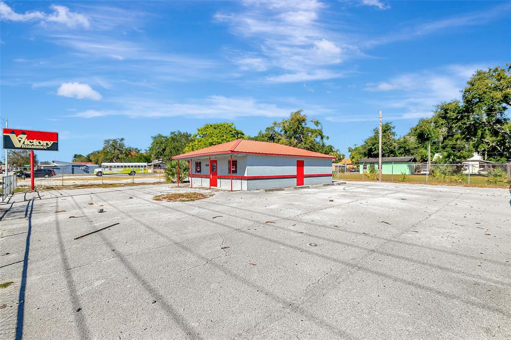 A single-story commercial building with a red roof stands in a large, paved parking lot — 305 & 309 W MEMORIAL BOULEVARD, LAKELAND, FL