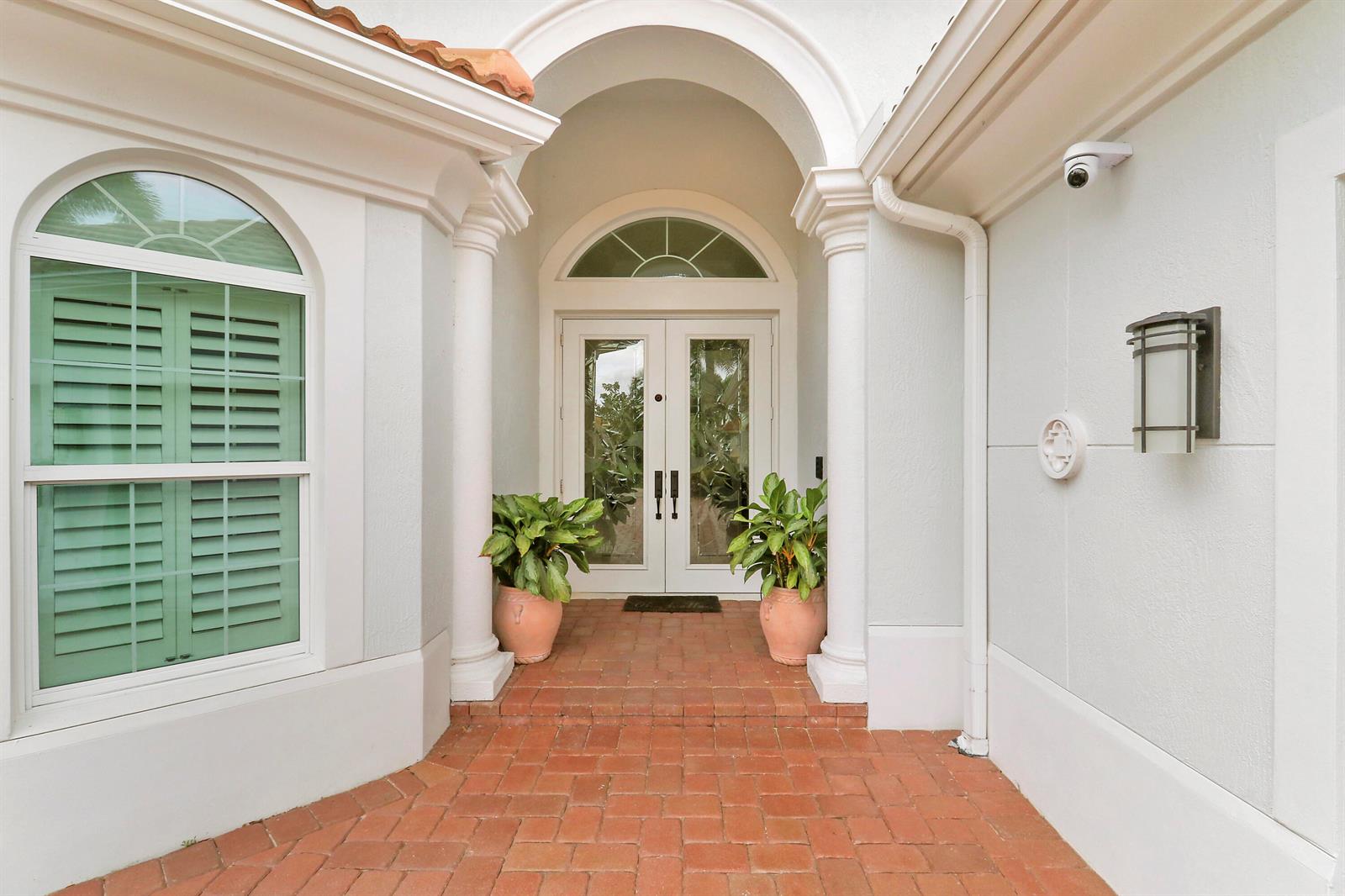 A brick walkway leads to a white double-door entrance framed by columns and potted plants — 236 Carina Drive, Jupiter FL 33478, JUPITER, FL
