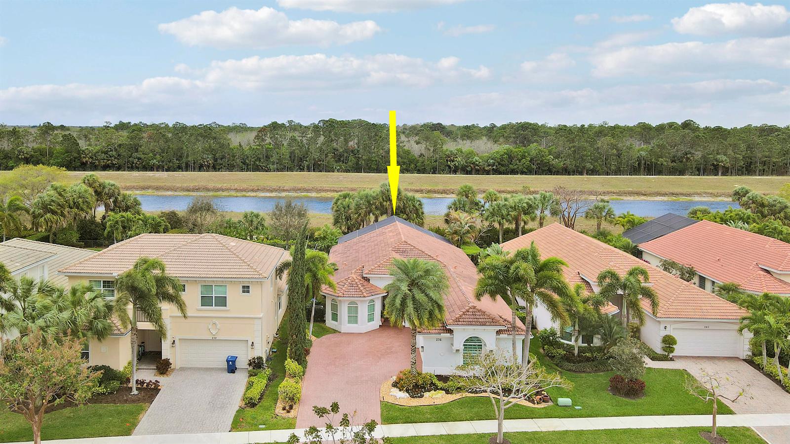 An aerial view shows a suburban house with a red-tiled roof facing a lake — 236 Carina Drive, Jupiter FL 33478, JUPITER, FL