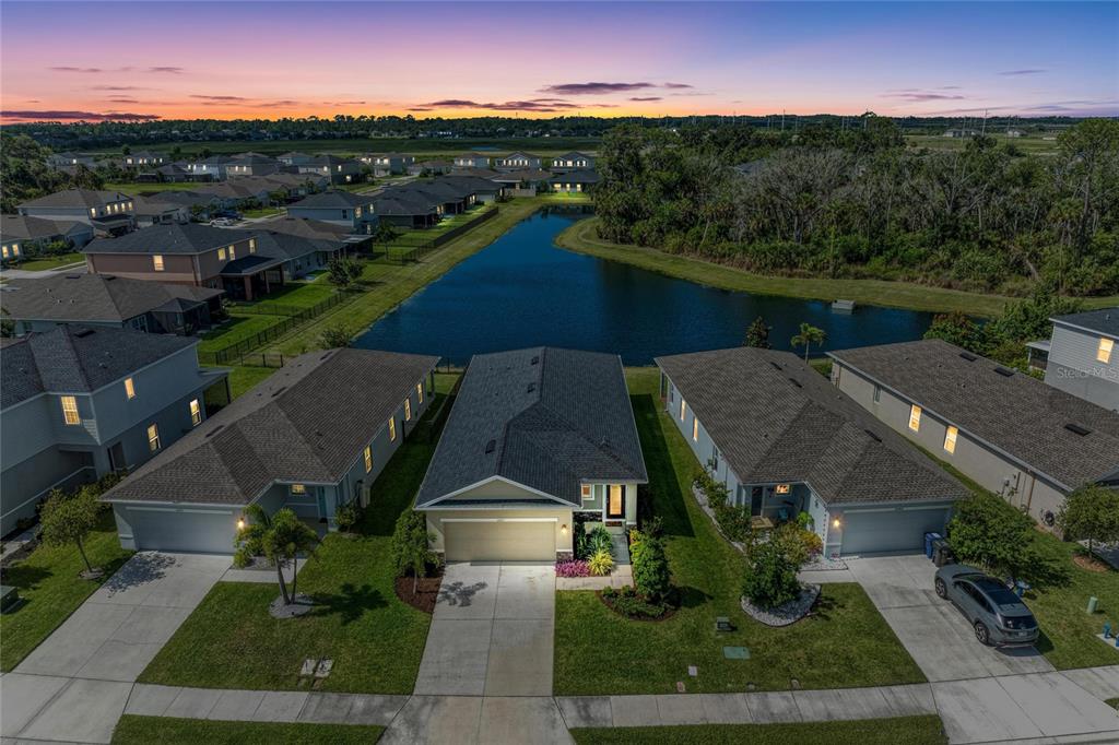 An aerial view shows three suburban houses with driveways facing a street and a pond — 10711 HIGH NOON TRL, PARRISH, FL