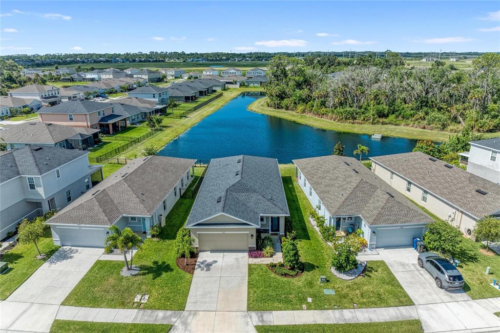 An aerial view shows three suburban houses with driveways facing a pond and neighborhood — 10711 HIGH NOON TRL, PARRISH, FL