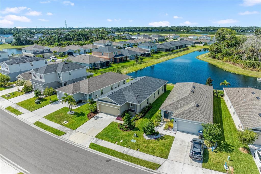 An aerial view shows a suburban neighborhood with houses, lawns, and a large retention pond — 10711 HIGH NOON TRL, PARRISH, FL