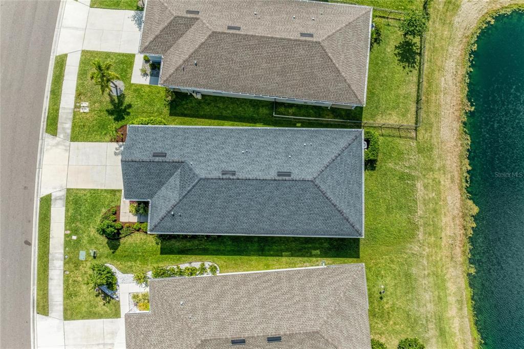 An aerial view shows three suburban houses with gray roofs situated next to a pond — 10711 HIGH NOON TRL, PARRISH, FL