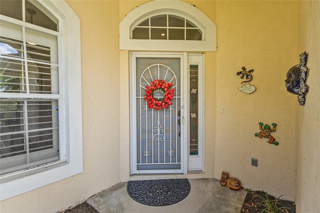 A front entryway features a white storm door with a tulip wreath and decorative wall art — 6662 OAKBROOKE CIRCLE, BRADENTON, FL