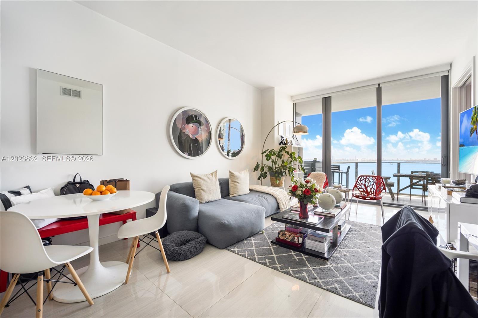 A modern living room features a grey sectional sofa, dining area, and floor-to-ceiling balcony windows — 480 NE 31st St # 1602, Miami FL 33137, MIAMI, FL