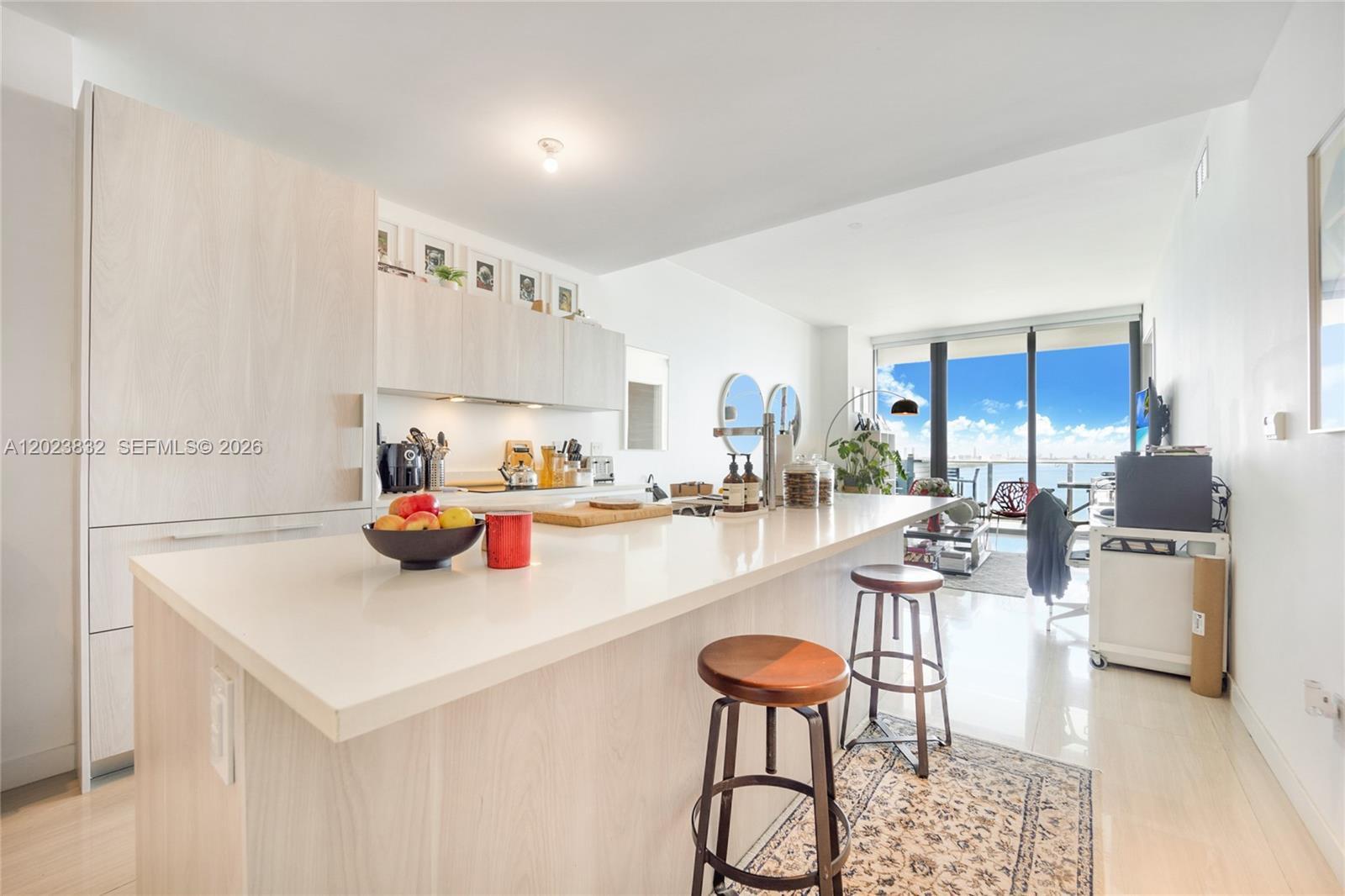 A modern kitchen features a white island with bar stools and a view of the ocean — 480 NE 31st St # 1602, Miami FL 33137, MIAMI, FL