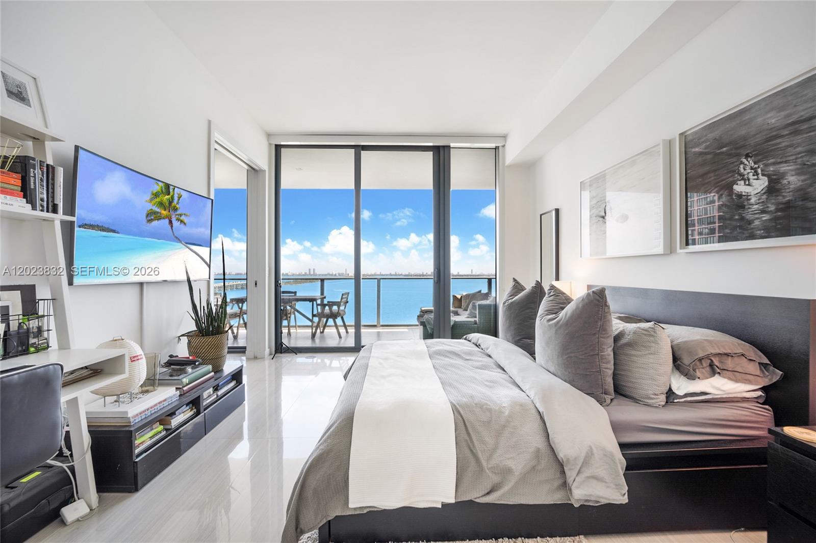 A modern bedroom features a bed, a wall-mounted television, and a balcony overlooking the ocean — 480 NE 31st St # 1602, Miami FL 33137, MIAMI, FL