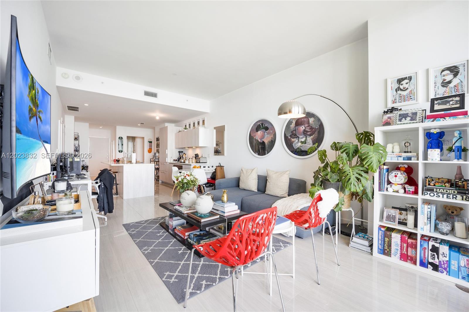 A modern living room features a gray sofa, red chairs, a coffee table, and white shelving — 480 NE 31st St # 1602, Miami FL 33137, MIAMI, FL
