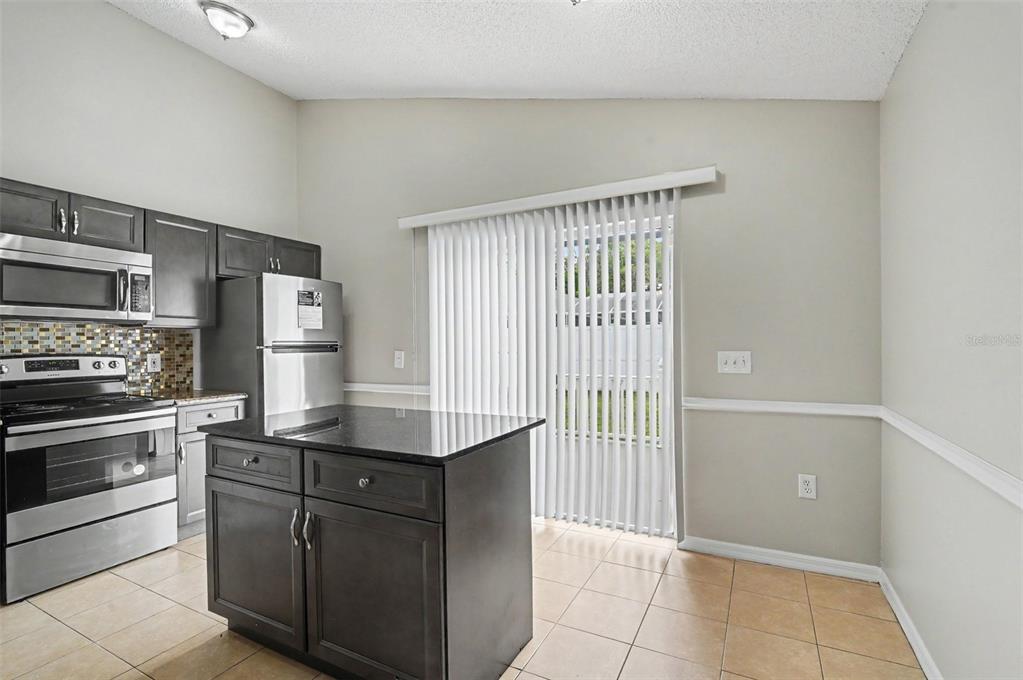 A kitchen features dark cabinets, stainless steel appliances, a center island, and sliding glass doors — 5655 NEW CAMBRIDGE ROAD, ORLANDO, FL