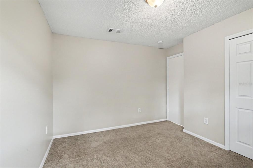 An empty bedroom features beige walls, tan carpeting, a textured ceiling, and a white door — 5655 NEW CAMBRIDGE ROAD, ORLANDO, FL