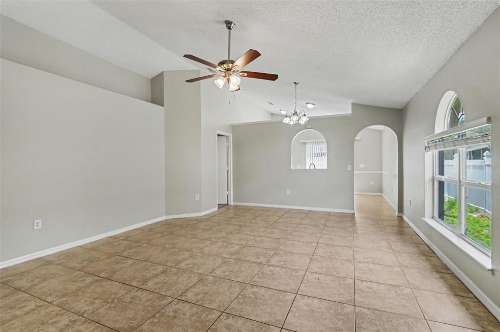 An empty living room features beige tile flooring, a vaulted ceiling, and a ceiling fan — 5655 NEW CAMBRIDGE ROAD, ORLANDO, FL