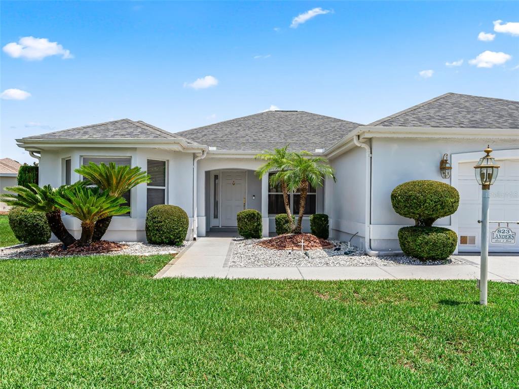 A single-story house with a white exterior, a gray shingled roof, and landscaped front yard — 823 SAN SALVADOR DRIVE, THE VILLAGES, FL