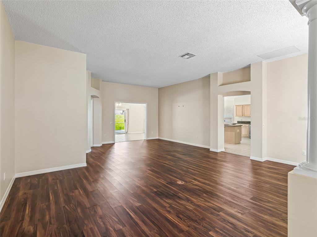 An empty living room features dark wood-look flooring, beige walls, and an arched entryway — 823 SAN SALVADOR DRIVE, THE VILLAGES, FL
