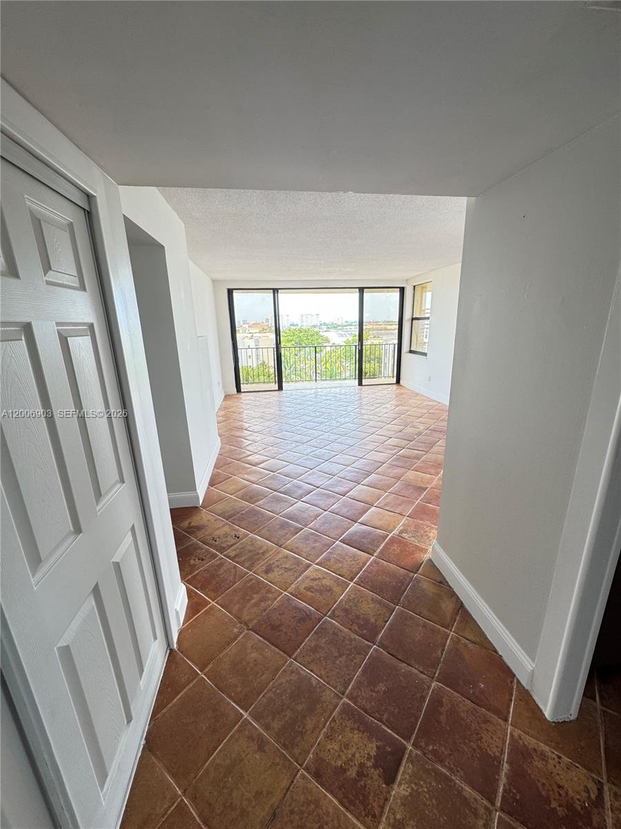 A room with terracotta tile flooring leads to a balcony with a city view — 1470 NE 123rd St # A701, North Miami FL 33161, NORTH MIAMI, FL