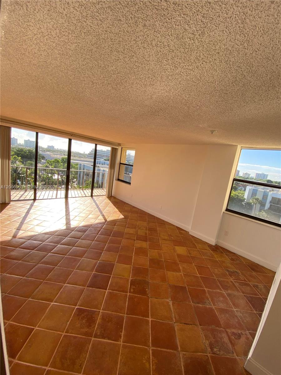 An empty room features terracotta tile flooring, a popcorn ceiling, and large sliding glass doors — 1470 NE 123rd St # A701, North Miami FL 33161, NORTH MIAMI, FL