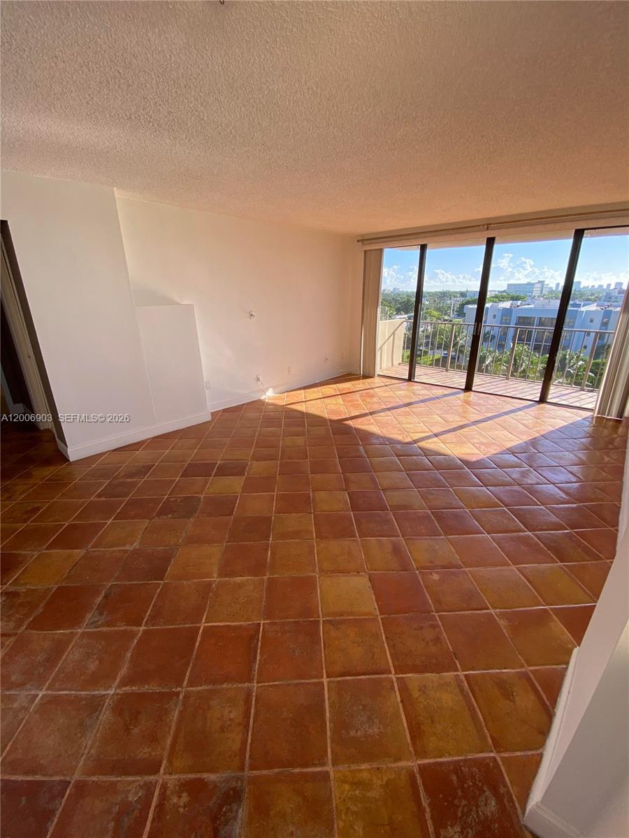 An empty living room features terracotta tile flooring and a sliding glass door to a balcony — 1470 NE 123rd St # A701, North Miami FL 33161, NORTH MIAMI, FL