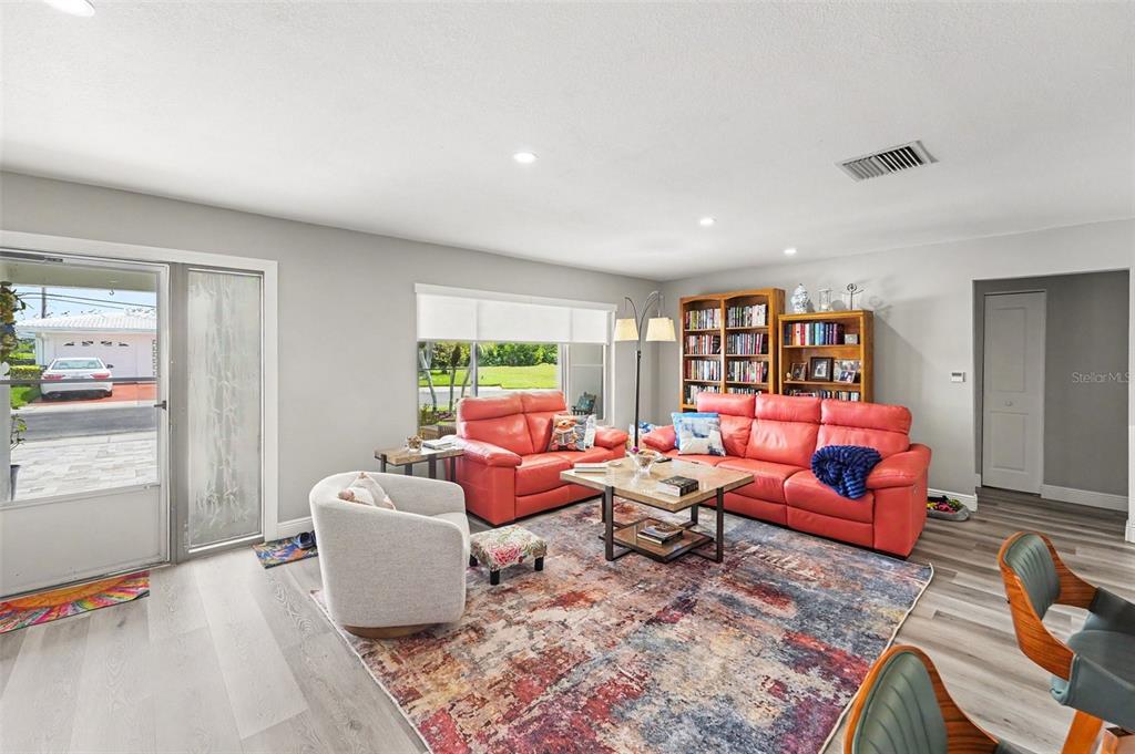 A living room features a red sofa, a light-colored armchair, and a patterned area rug — 3450 101ST TERRACE N, PINELLAS PARK, FL