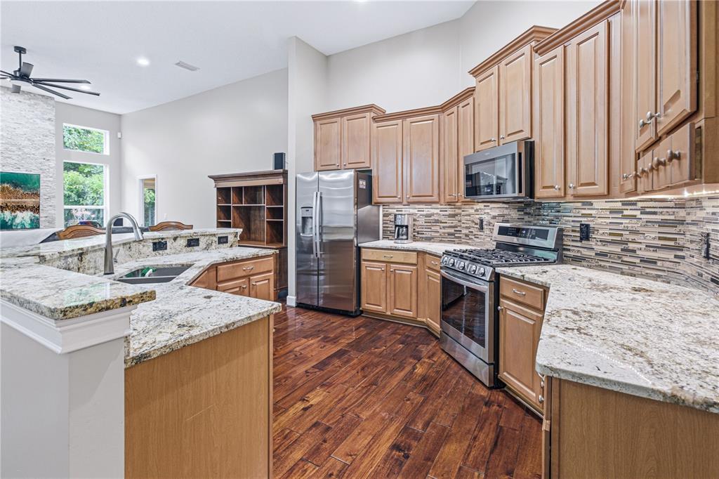 A kitchen features light wood cabinets, granite countertops, stainless steel appliances, and dark hardwood floors — 14473 MAGNOLIA SPRINGS LANE E, JACKSONVILLE, FL