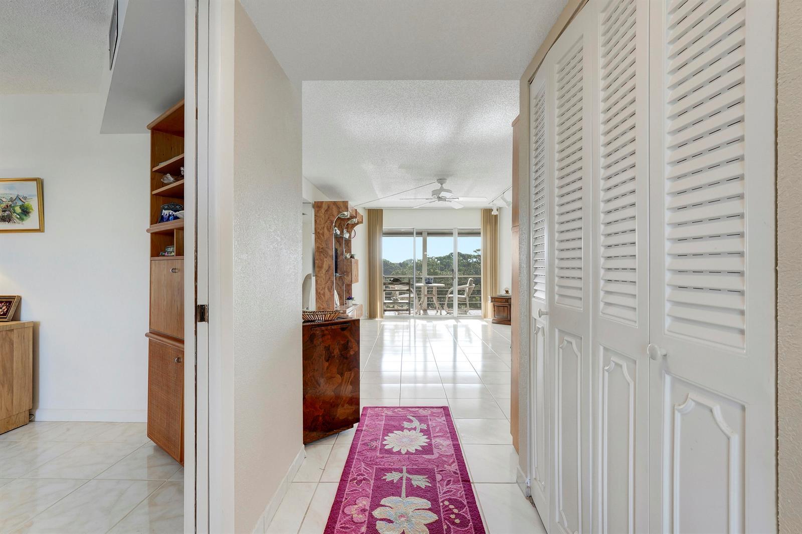 A hallway with a pink floral runner leads to a bright living area with balcony access — 3597 Birdie Drive # 607, Lake Worth FL 33467, LAKE WORTH, FL