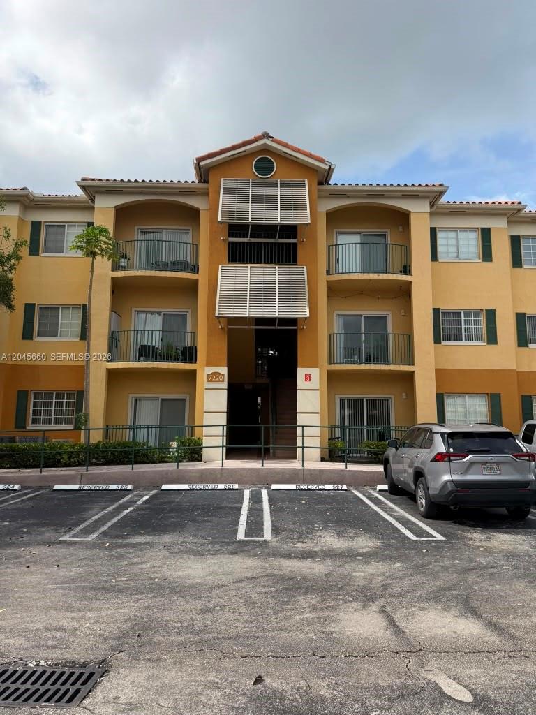 A three-story apartment building with yellow stucco walls, balconies, and a parking lot in front — 7220 NW 114th Ave # 105, Doral FL 33178, DORAL, FL