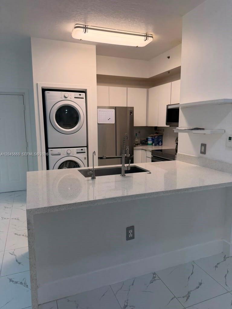 A kitchen features white cabinets, stainless steel appliances, a stacked washer-dryer, and a quartz island — 7220 NW 114th Ave # 105, Doral FL 33178, DORAL, FL