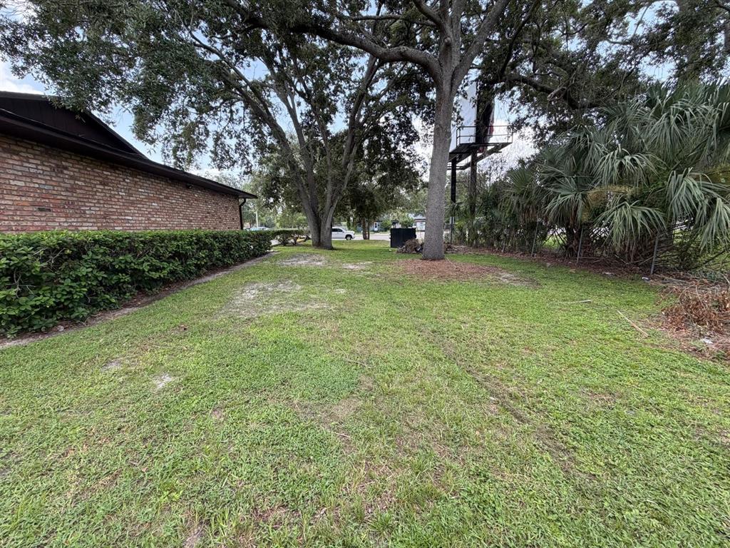 A grassy yard sits beside a brick building under large shade trees — N JOHN YOUNG PARKWAY, KISSIMMEE, FL