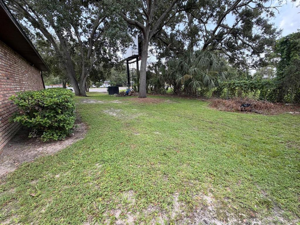 A grassy backyard features a brick house wall, large trees, and a metal billboard structure — N JOHN YOUNG PARKWAY, KISSIMMEE, FL