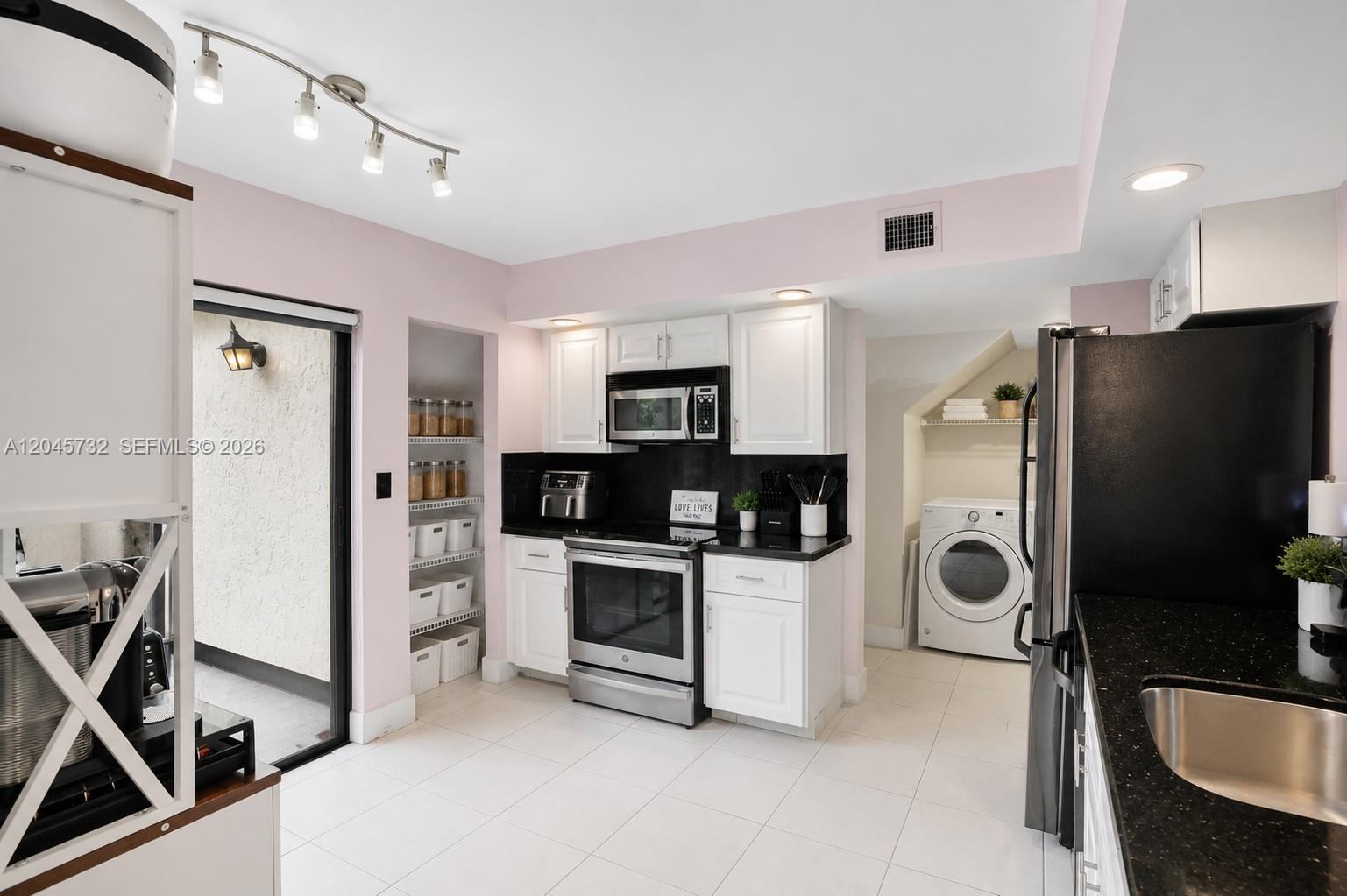 A kitchen features white cabinets, black countertops, stainless steel appliances, and an adjacent laundry area — 7758 La Mirada Dr # 7758, Boca Raton FL 33433, BOCA RATON, FL