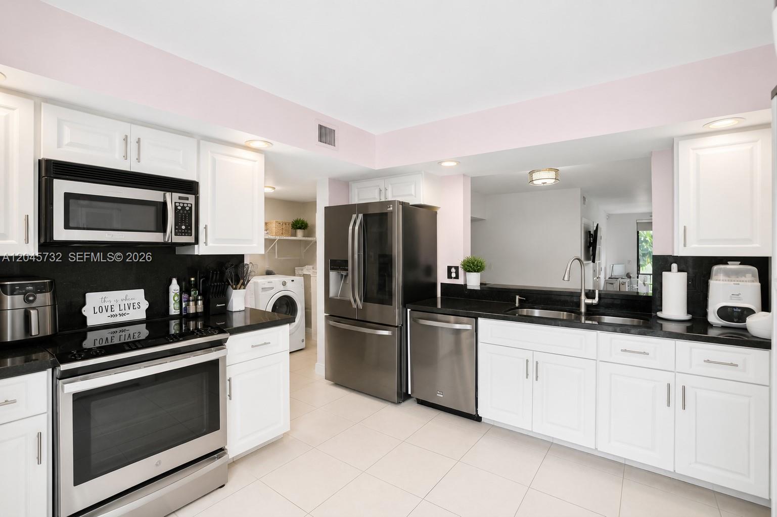 A kitchen with white cabinets, black countertops, stainless steel appliances, and an adjacent laundry area — 7758 La Mirada Dr # 7758, Boca Raton FL 33433, BOCA RATON, FL