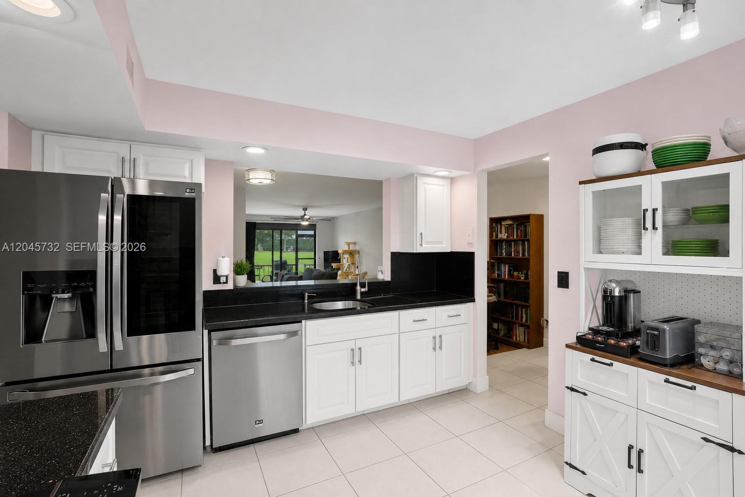 A kitchen features white cabinets, black countertops, stainless steel appliances, and a pass-through window — 7758 La Mirada Dr # 7758, Boca Raton FL 33433, BOCA RATON, FL