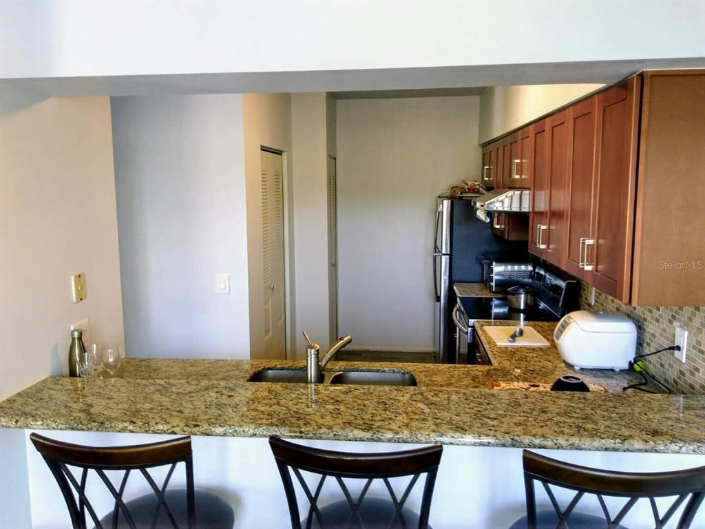 A kitchen with granite countertops, wooden cabinets, and a breakfast bar with stools — 3366 MERMOOR DRIVE UNIT 206, PALM HARBOR, FL