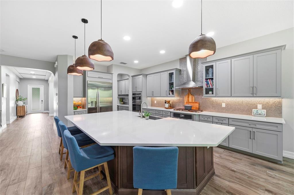 A modern kitchen features a large white island, gray cabinets, and blue bar stools — 4441 ALBERO PLACE, WESLEY CHAPEL, FL