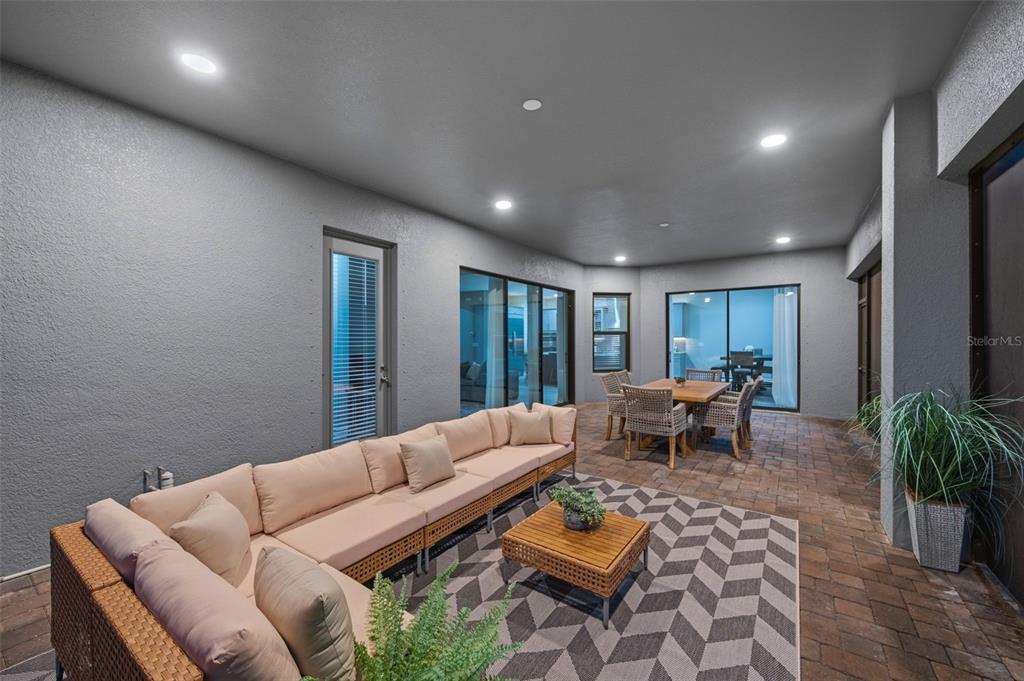 A covered outdoor patio features a large sectional sofa, dining set, and patterned area rug — 4441 ALBERO PLACE, WESLEY CHAPEL, FL