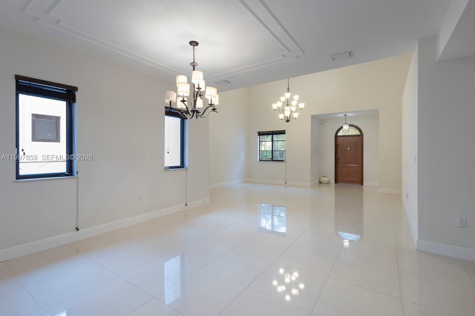 A bright, empty room features white tile floors, two chandeliers, and a wooden front door — 324 SW 30th Rd, Miami FL 33129, MIAMI, FL