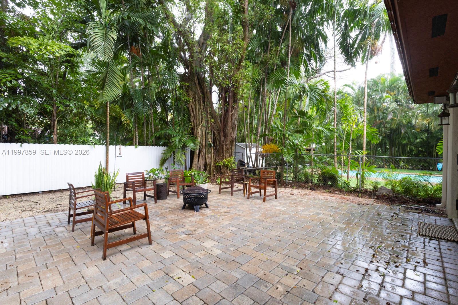 A paved patio features wooden chairs and a fire pit surrounded by lush tropical trees — 324 SW 30th Rd, Miami FL 33129, MIAMI, FL