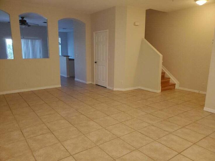 An open living area features beige tile flooring, arched wall cutouts, and a wooden staircase — 158 Village Boulevard # D, Tequesta FL 33469, TEQUESTA, FL