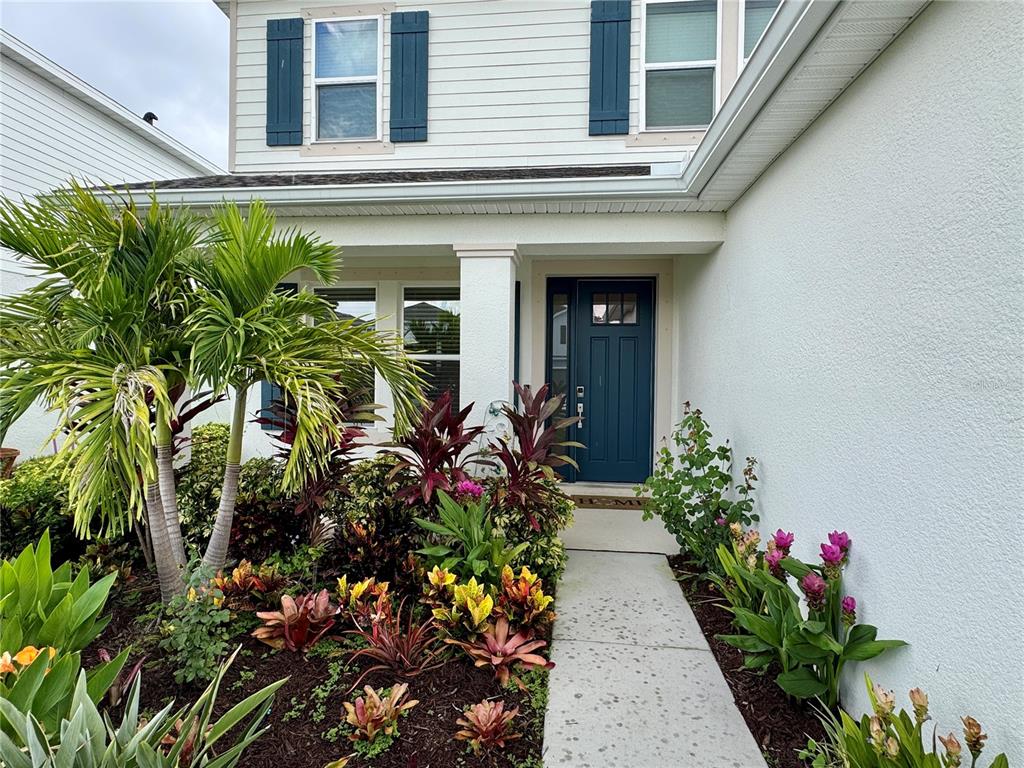 A blue front door is framed by a landscaped garden and a concrete walkway — 4334 POND BROOK COURT, BRADENTON, FL