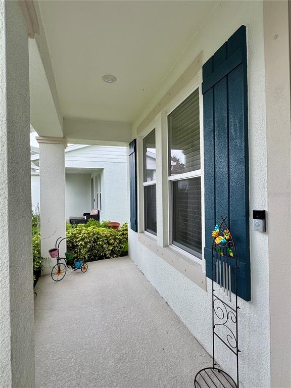 A covered front porch features a concrete floor, blue shutters, and a decorative wind chime — 4334 POND BROOK COURT, BRADENTON, FL