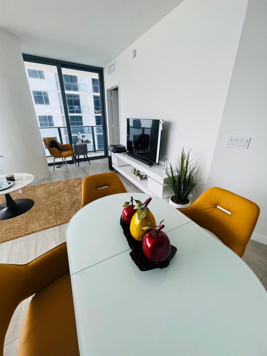 A dining area with a white table and yellow chairs overlooks a balcony and city buildings — 55 SW 9th St # 3308, Miami FL 33130, MIAMI, FL