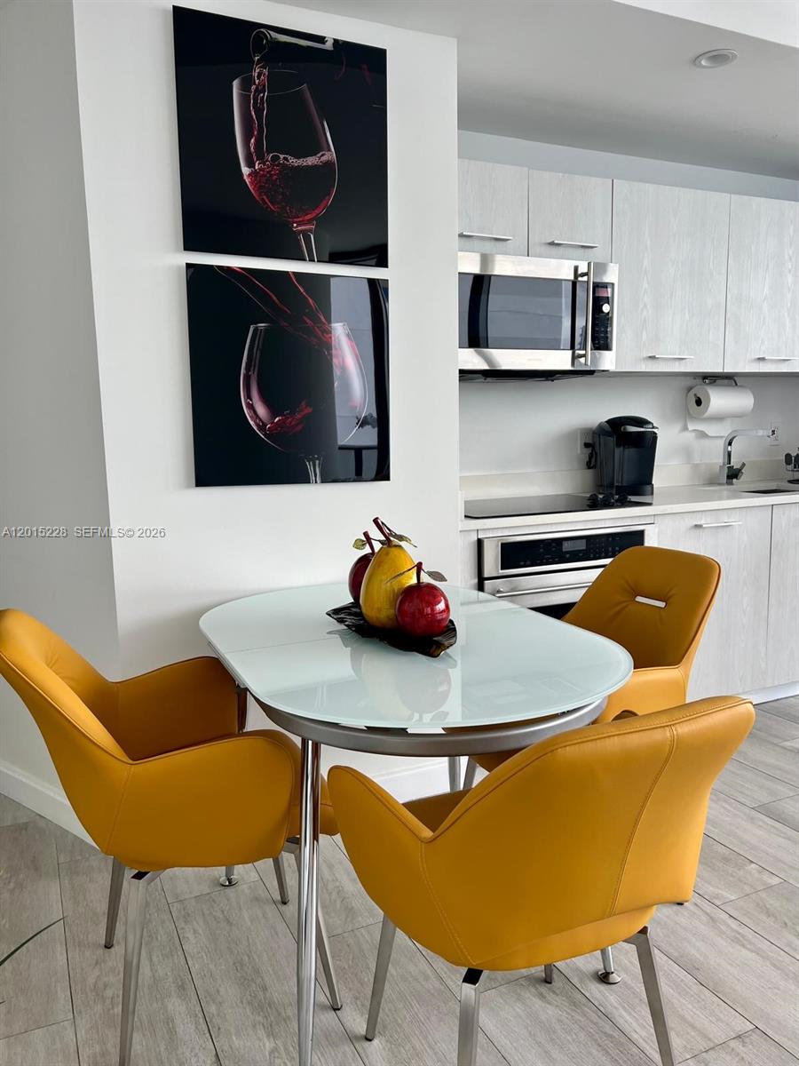 A dining area features a glass-topped table, yellow chairs, and wall art near a kitchen — 55 SW 9th St # 3308, Miami FL 33130, MIAMI, FL