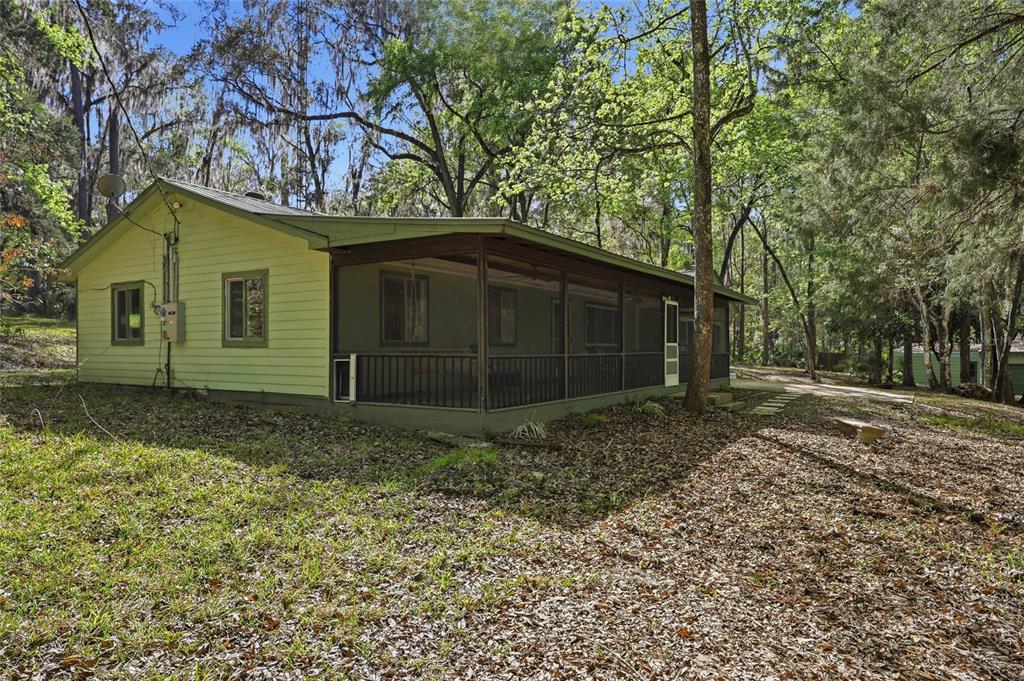 A light yellow house with a large screened-in porch sits in a wooded yard — 8856 NW 230TH STREET, MICANOPY, FL