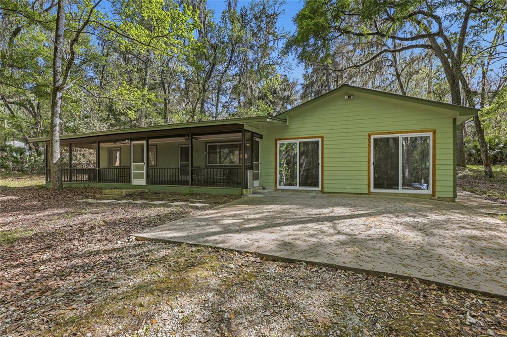 A light green house with a screened-in porch and a concrete patio in a wooded area — 8856 NW 230TH STREET, MICANOPY, FL