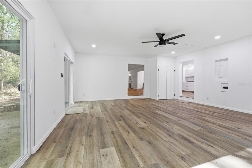 A spacious, white-walled living room features wood-look flooring, a ceiling fan, and sliding glass doors — 8856 NW 230TH STREET, MICANOPY, FL