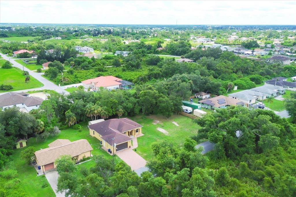 An aerial view shows a suburban neighborhood with houses, green lawns, and dense surrounding trees — 431 SEVILLA STREET, NORTH PORT, FL